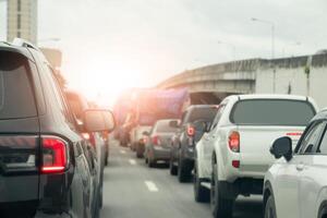 Rear side of car stop and trun on brake light on the asphalt road. Many car parking and queuing during traffic jams at intersections. Beside car with cement overpass bridge. Under bright sky. photo