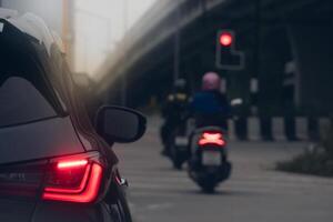 Rear side of dark car stop and turn on brake light. Motorcycle drives forward. Parallel concrete bridges are in front. Environment of traffic on the road at evening. photo