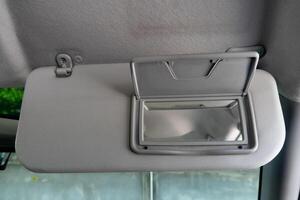 Son visors of car with open close the glass panel. Front view of the driver inside car. Background out of car by cement wall under shadow of tree. photo