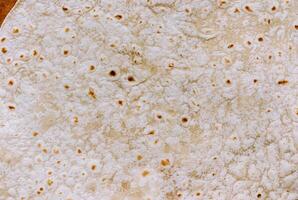 Detailed close-up of a tortilla bread surface showing its unique texture and golden brown spots, perfect for food backgrounds and culinary projects. photo