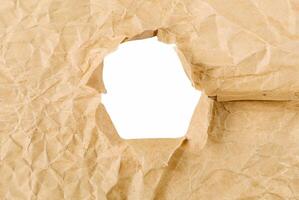 Close-up of crumpled brown paper with a torn hole, creating a frame effect on a white background, ideal for creative design use. photo