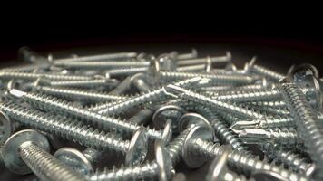 This shows a close up view of deck screws in a pile. The screws are all silver and have a flat head. The is taken from a very close perspective, camera moves. video