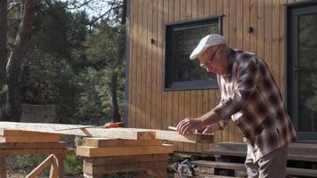 In a peaceful outdoor setting, a talented craftsman meticulously works on a wooden structure. An elderly man marks a wooden beam for further processing. video
