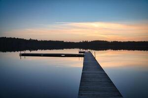Wooden jetty at sunset on a Swedish lake. The colors are reflected in the water photo