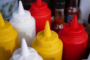 At a bustling food stand, a wide array of condiment bottles featuring vibrant colors can be found photo