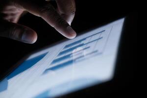 Closeup of a hand interacting with a digital tablet showing various data charts and info photo