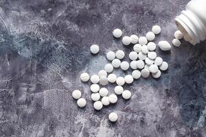 Various Scattered White Tablets from an Open Medication Bottle Placed on a Surface Area photo