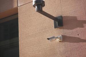 A visibly damaged security camera is mounted on a wall with its bracket still attached photo