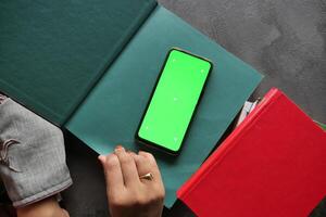 A smartphone placed atop books, set against a vibrant green background designed for creative mockups photo