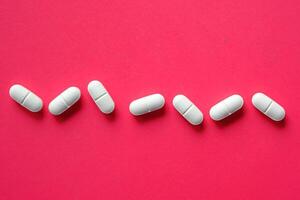 An Array of White Capsules Neatly Arranged Against a Bright and Vibrant Pink Background photo
