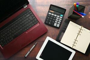 A modern office workspace featuring a laptop, tablet, calculator, and a notepad for tasks photo