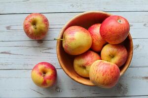 A bowl of fresh red apples beautifully arranged on a rustic wooden table surface photo