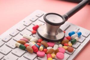A stethoscope and some pills resting on a computer keyboard illustrate a health concept photo
