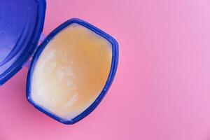 A container filled with moisturizing petroleum jelly displayed against a soft pink background photo