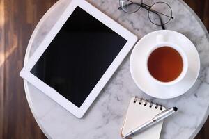 A cozy workspace with a tablet, warm tea, and a notepad on a beautiful marble table photo