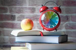 A colorful alarm clock and fresh apple on books, set against a stylish brick background photo
