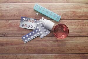 An assortment of various medications displayed with a weekly pill organizer on a wooden table photo