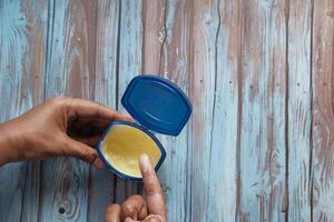 A CloseUp of a Hand Skillfully Applying Cream from an Open Container on a Wooden Table photo