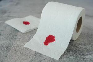 A blood spot is noticeable on a tissue next to a roll of toilet paper in the background photo