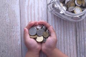 Two Hands Holding a Variety of Coins Next to a Glass Jar Overflowing with Loose Change photo