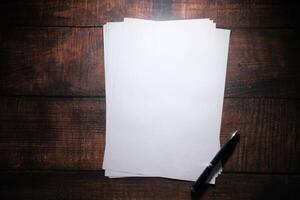 A series of blank sheets of paper and a pen neatly placed on a wooden table surface photo