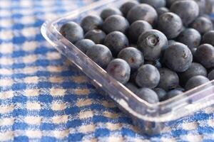 A Clear Container Filled with Fresh Blueberries Placed on a Checkered Tablecloth Pattern photo