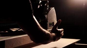 Close-up of a man cuts a wooden plank with an electric circular saw in a workshop. Cutting a piece of wood on a circular saw in backlight. Ideal topics related carpentry, efficient sawing techniques video