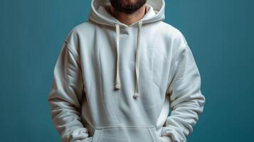 A man is wearing a white hoodie and is standing in front of a blue wall photo
