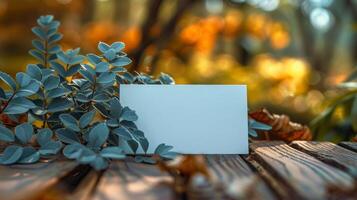 A white card is on a wooden table with leaves and a leafy green plant photo