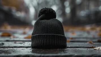 A black knit hat with a pom pom sits on a wet sidewalk photo