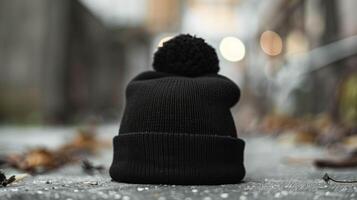 A black hat with a pom pom on top is sitting on a sidewalk photo