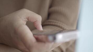 A closeup of a hand skillfully using a smartphone with a softly focused background video