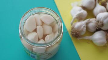 Garlic Cloves Stored in a Jar Alongside Fresh Garlic Bulbs Set Against a Colorful Background video