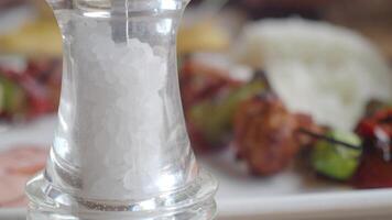 A closeup of a salt shaker next to grilled skewers with rice in the background video