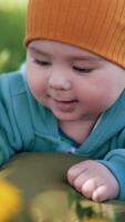 Smiling toddler in warm clothes and cap enjoys staying outside. Adorable little boy resting on the mattress in nature. Close up. Vertical video