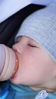 Lovely little baby boy is fed from a bottle. Caucasian child falling asleep in a stroller while eating from a bottle. Vertical video