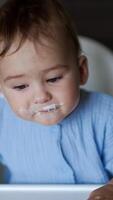 Tiny kid is fed by his mom. Sweet happy baby boy rejoices smiling adorably and showing his two lower teeth. Close up. Vertical video