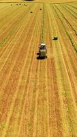 Agricultural machinery pressing green grass in the field. Harvester and tractor in field press grass into bundle in a sunny day. Aerial view. Vertical video