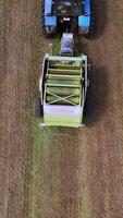 Ready grass bale comes out of a pressing machine. Agricultural machinery presses grass to make round bundle in the field. Top view. Vertical video