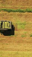 Top view of tractor pressing grass in the field. Aerial view of one round bale and agricultural machine working on a green meadow. Camera moves bottom up. Vertical video