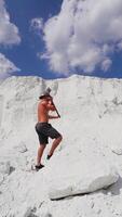 Muscular man on the background of white mountain. Shirtless guy with iron hammer on the natural background of large mountain in summer. Vertical video