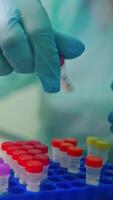 Laboratory worker in protective gloves is checking test tubes. Vials with liquid with colorful covers on a support in a laboratory. Vertical video