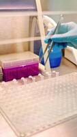 Hand of laboratory worker with tweezers on the table. Assistant putting empty sterile vials into the rack with tweezers in research clinic. Vertical video