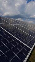 fechar-se do solar painel debaixo a nublado céu. alternativo fonte do energia. azul solar célula painel em verde grama. lento movimento. vertical video