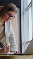 Office lady surfing the net and taking notes. Female employee standing leaned on the table in a spacious office. Vertical video