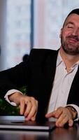 Smiling good-looking bearded man opens his laptop. Man changes in face when he can't open his computer. Blurred backdrop. Vertical video
