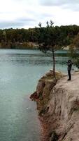 Man standing on shore. Aerial view of man standing on lake shore and taking photo of nature Vertical video