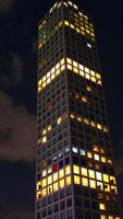 Top of the skyscraper with lights in the windows. Drone footage rising along the building at the backdrop of dark night sky with clouds. Vertical video