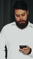 Portrait of man with phone. Bearded stylish business man typing message on mobile phone Vertical video