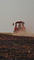 Brown field background and a tractor plowing the soil. Tractor cultivating the field, preparing land for sowing in the farmland. Vertical video